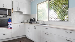A modern kitchen with white cabinets, a microwave, a toaster, and a window with a view of greenery.