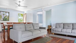 A modern living room with two grey sofas, wooden dining table, and a ceiling fan.