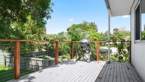 A wooden deck with a barbecue grill, surrounded by a metal fence and lush greenery.