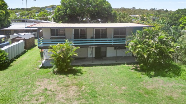 A two-story house with a balcony, surrounded by a grassy yard and palm trees.