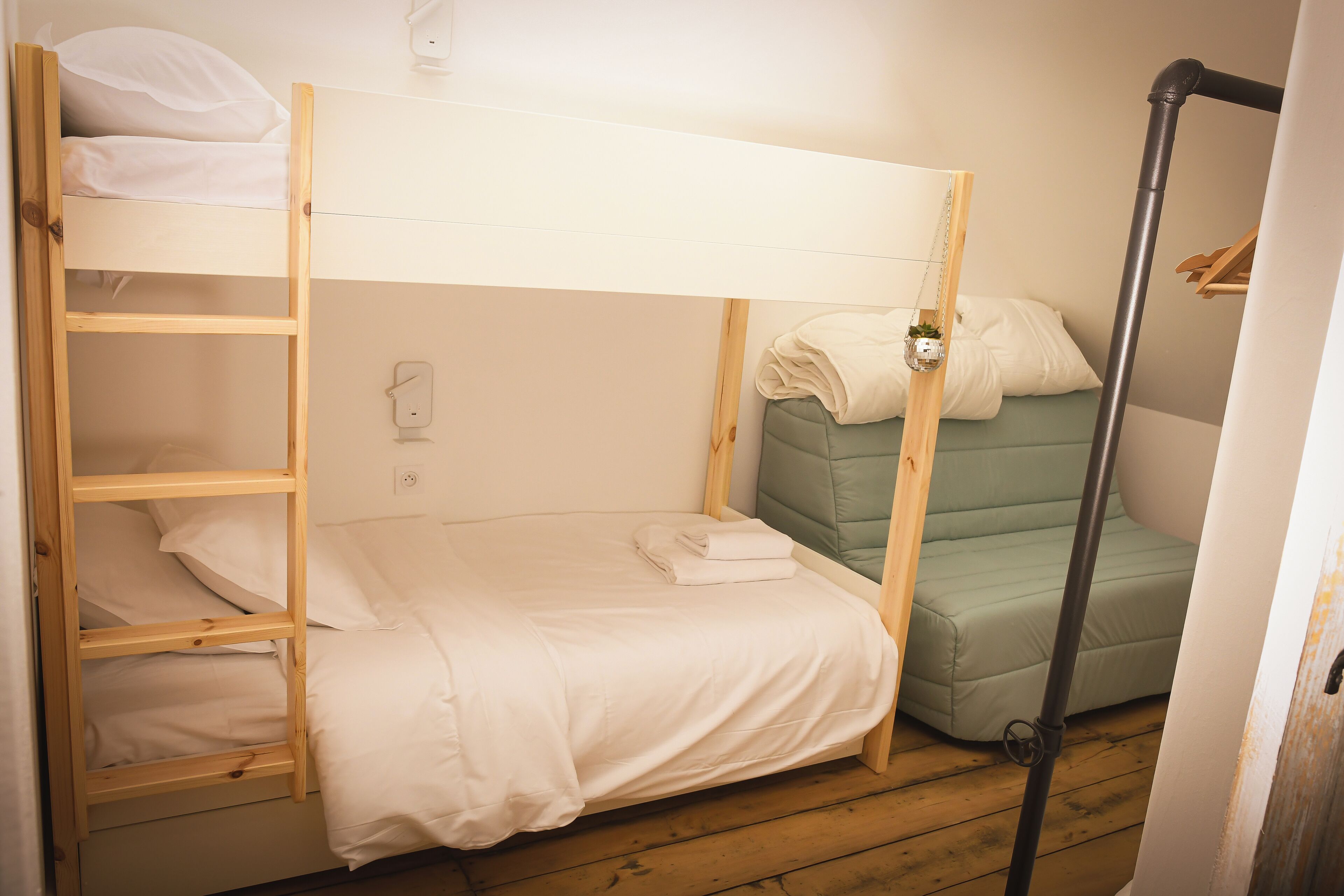 Camera con letto a castello, una scala in legno, un divano verde e una presa elettrica bianca.
