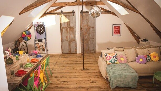 A cozy attic room with a wooden floor, a sofa with colorful pillows, a dartboard, and a disco ball. - Magnificent Festive Loft (Saint-Pourçain-sur-Sioule)