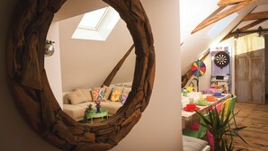 A room with a large wooden arch, a sofa with colorful cushions, a small table with a plant, and a dartboard on a wall. - Magnificent Festive Loft (Saint-Pourçain-sur-Sioule)
