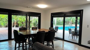 A dining area with a wooden table and chairs, large sliding glass doors leading to a pool and outdoor area. - Serene Getaway – Quiet Oasis with Pool & Rain Showers (Harlingen)