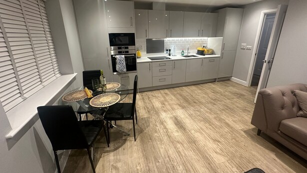 A modern kitchen with grey cabinets, a dining table with chairs, and a sofa in the living area. - Chic and spacious 2 bedroom, 2 bath Apartment (Epsom)