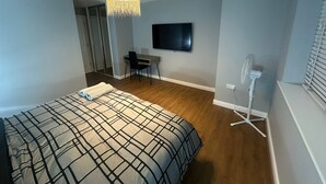 A bedroom with a bed, a desk, a chair, a TV, and a ceiling fan. - Chic and spacious 2 bedroom, 2 bath Apartment (Epsom)