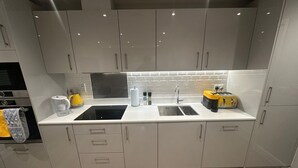 A modern kitchen with grey cabinets, a black induction cooktop, a double sink, and a yellow toaster. - Chic and spacious 2 bedroom, 2 bath Apartment (Epsom)