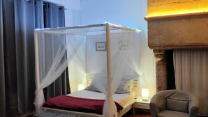 Una habitación con una cama bajo un dosel blanco, una mesita de noche con una lámpara y dos sillas.