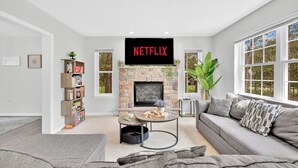 Ett vardagsrum med en öppen spis i sten, en Netflix-logotyp ovanför tv:n, en grå soffa och en bokhylla med brädspel.
