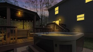 Ett bubbelbad på ett trädäck med ett takförsett sittområde och ett hus i bakgrunden.