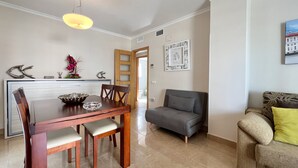 Un coin repas avec une table et des chaises en bois, un canapé gris et un petit fauteuil agrémenté d’un coussin jaune.