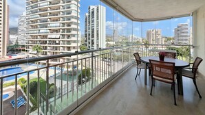 Un balcon avec une table et des chaises, donnant sur une piscine et des immeubles de grande hauteur.