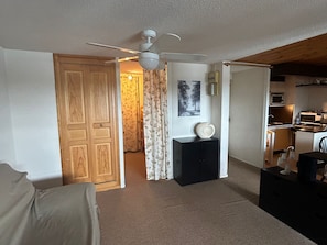 A compact living space with a ceiling fan, a kitchen area with a microwave, and a door leading to another room.
