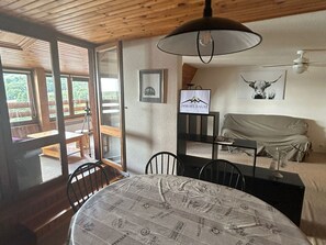 Um quarto com teto de madeira, uma mesa redonda com toalha de mesa estampada, uma cama com cobertor, um quadro emoldurado e uma placa na parede.