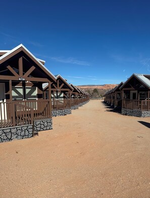 A row of cabins with stone railings and a dirt path leading to them. - Arches Hut (Moab)