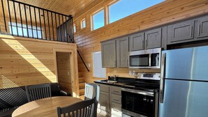 A modern kitchen with wooden cabinetry, a stainless steel refrigerator, and a dining area with a round table and chairs. - Arches Hut (Moab)