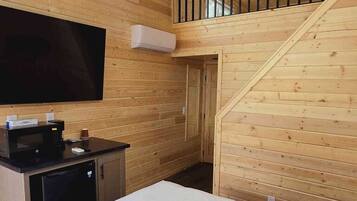 A wooden interior with a ceiling fan, a flat-screen TV, a kitchen area with a microwave, and a staircase to an upper level.