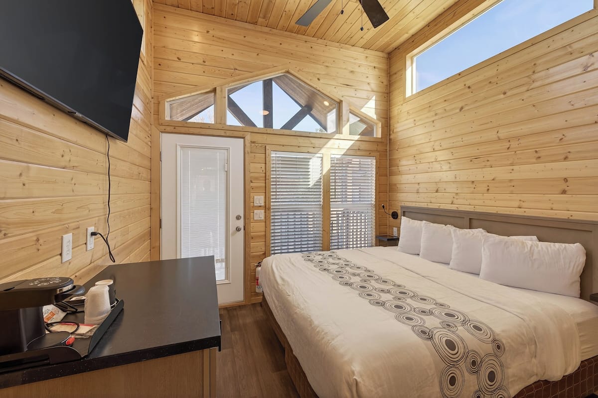 Ein Zimmer in einer Holzhütte mit einem Bett, einem Schreibtisch und einem Fernseher.