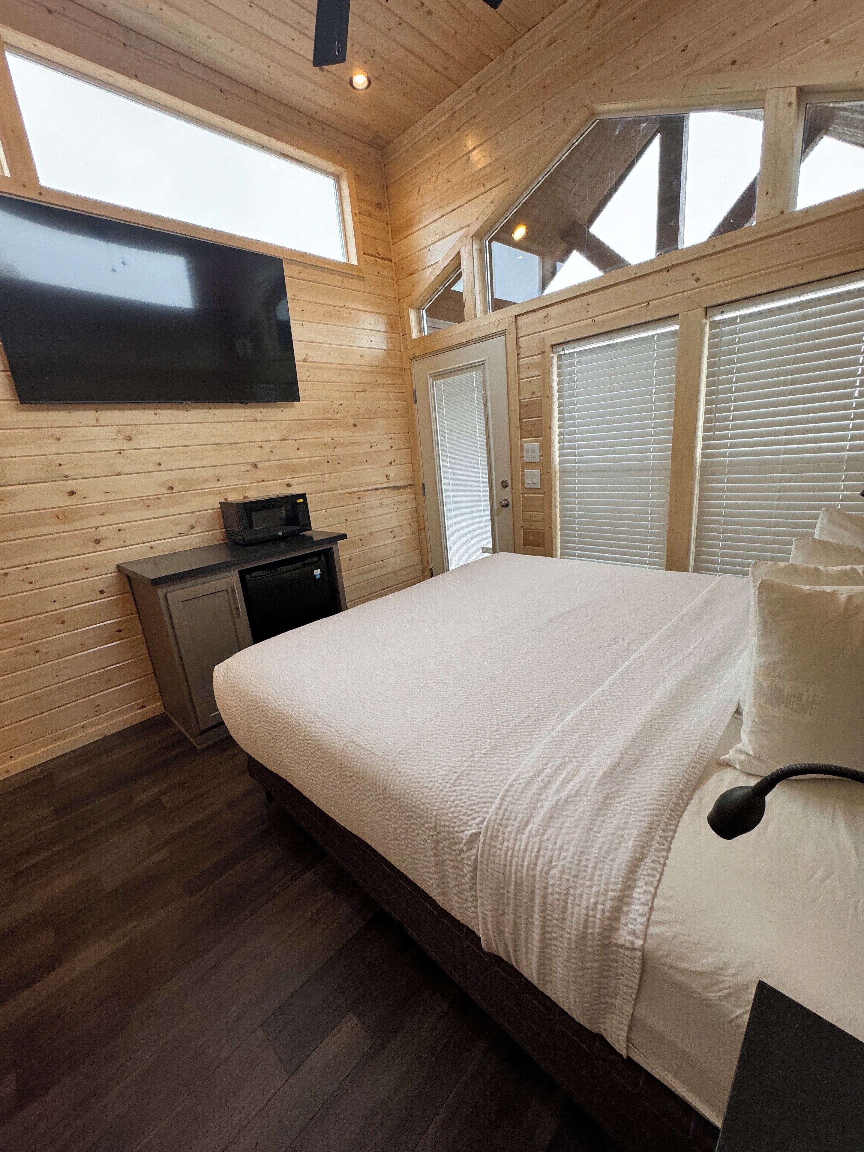 A bedroom with a large bed, wooden walls, a flat-screen TV, and a small kitchenette.