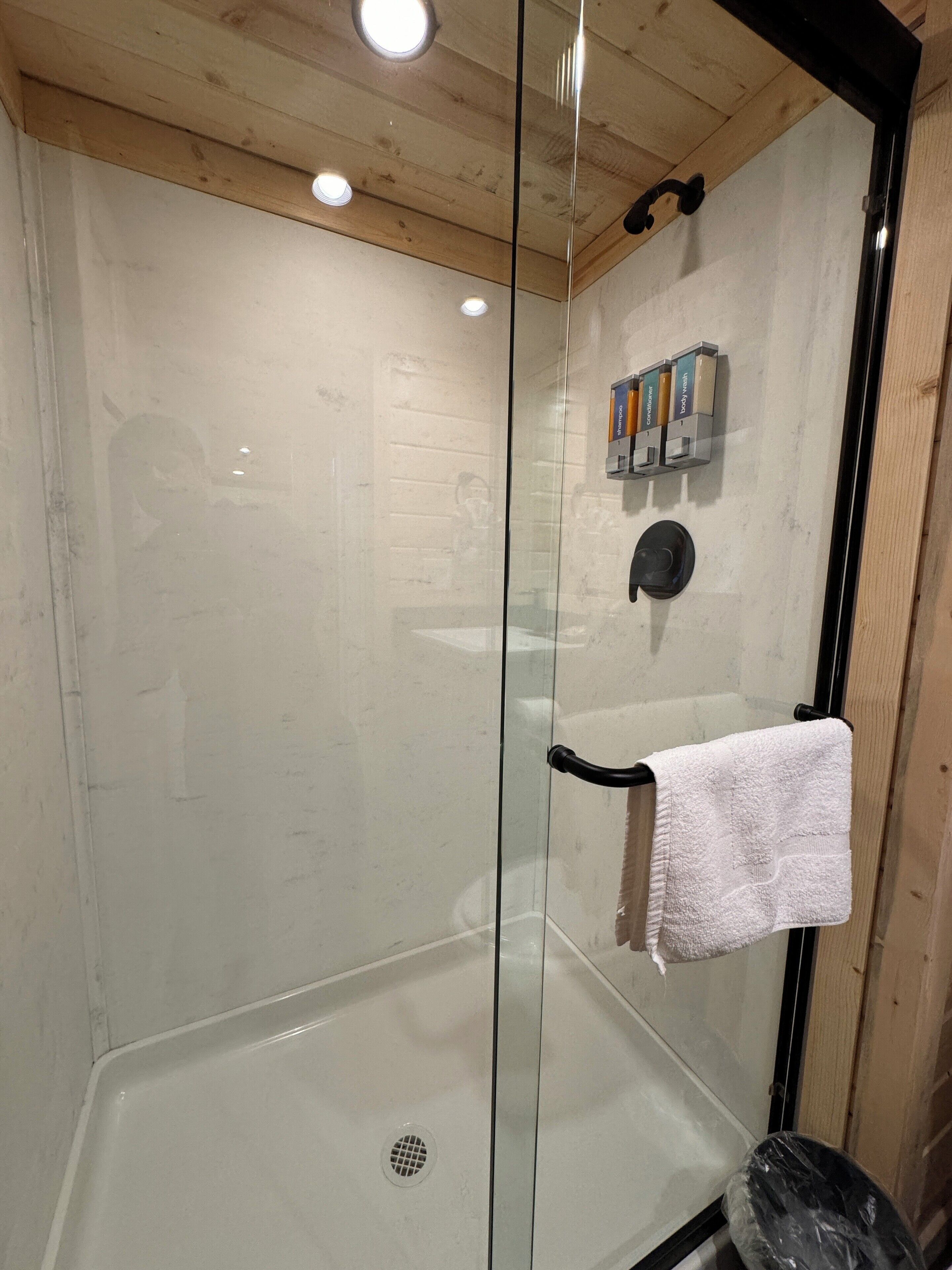 A glass-enclosed shower with a white towel hanging on a black towel rack.