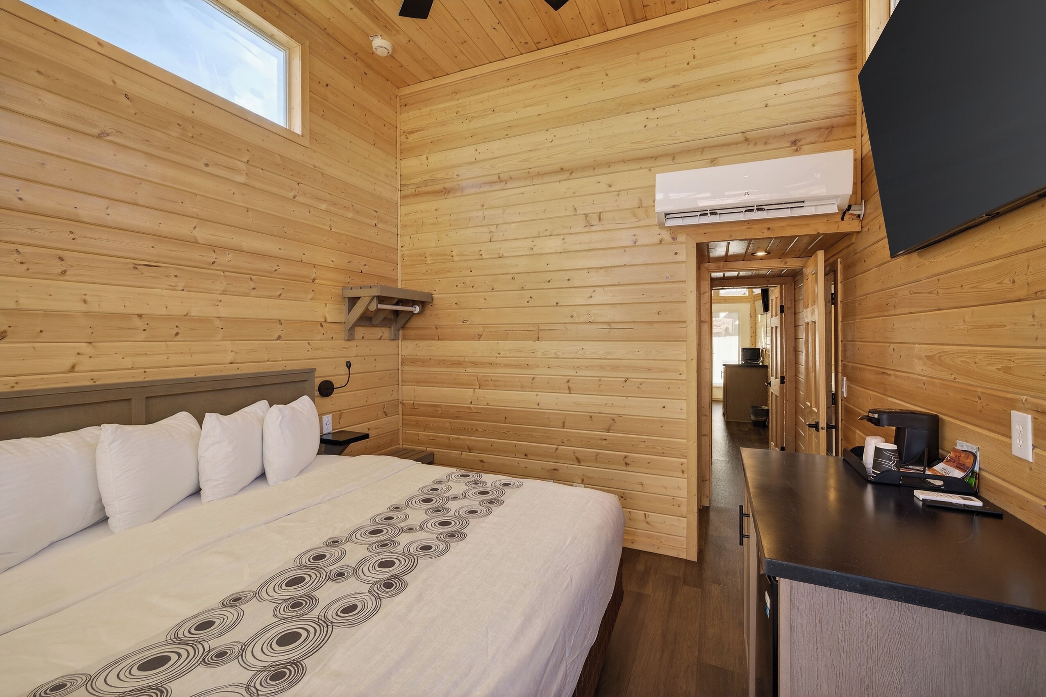 Ein Zimmer in einer Holzhütte mit einem Bett, einem Schreibtisch und einem an der Wand befestigten Fernseher.