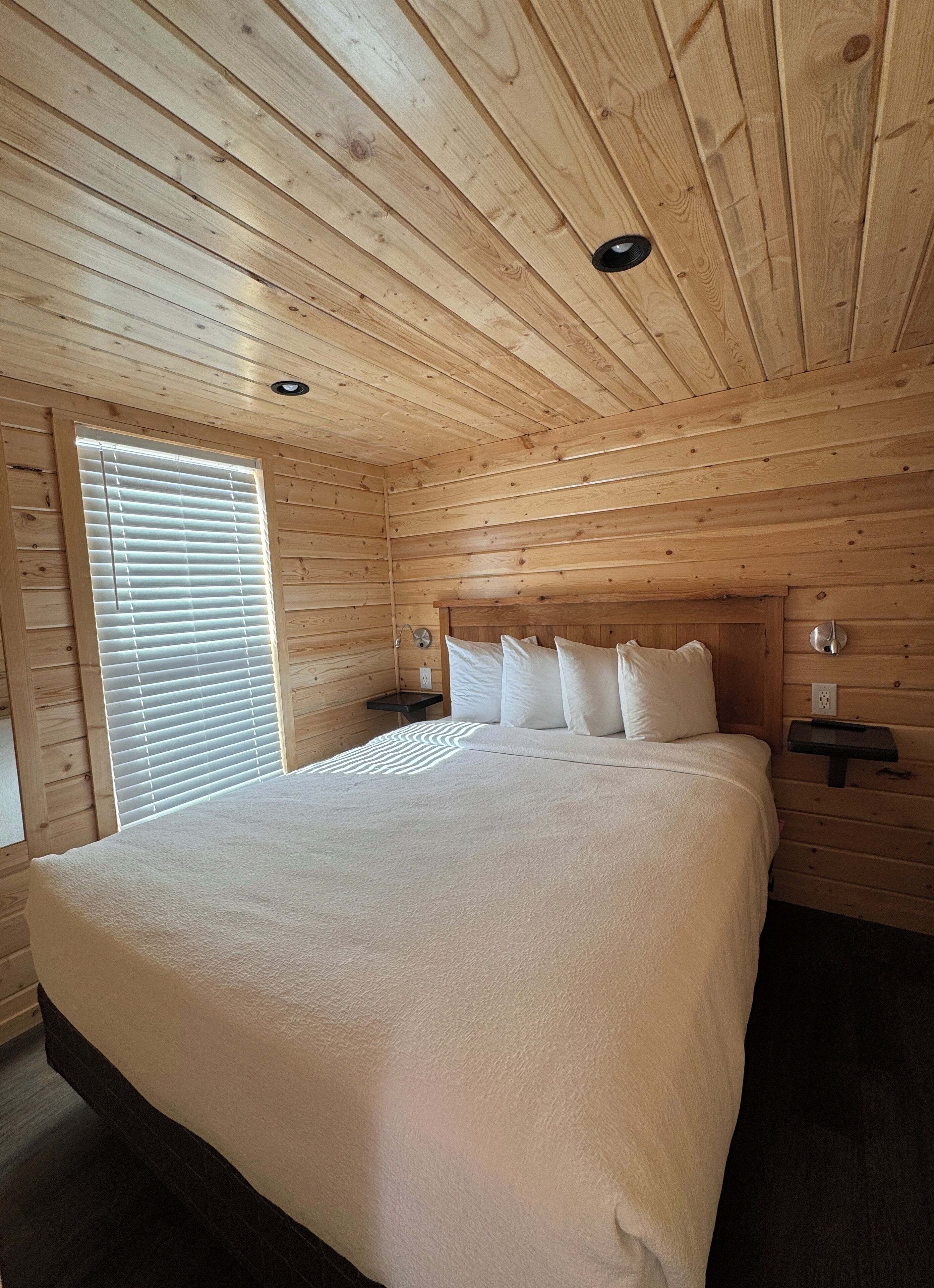 A wooden-paneled bedroom with a large bed, bedside tables, and a window with blinds.