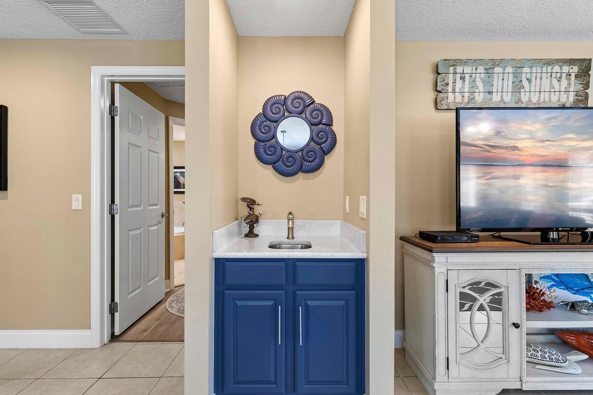 Una cocina con armarios azules, un lavamanos y un espejo decorativo. Hay un letrero sobre el espejo que dice "LET'S DO SUNSET".