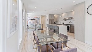 Una cocina moderna con electrodomésticos de acero inoxidable, una mesa de comedor de vidrio y vistas de la ciudad a través de amplias ventanas.