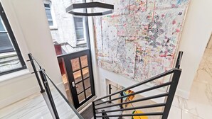 Un interior moderno con una escalera, un cuadro abstracto grande en la pared y vistas al exterior.