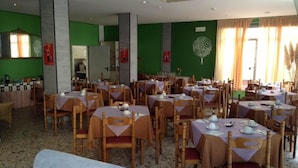 Un espace repas comprenant plusieurs tables et chaises, des murs verts et un élément décoratif mural.