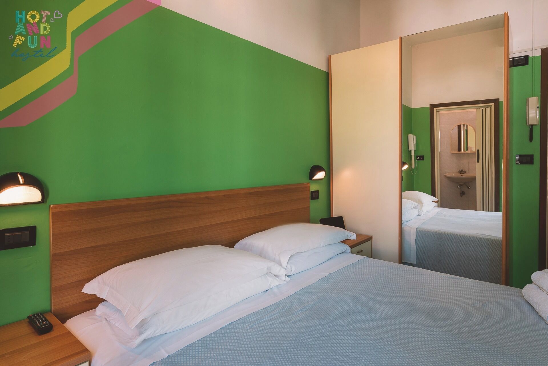 A hotel room with a green wall, a wooden headboard, and a large mirror.