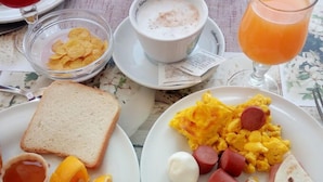 Une table dressée pour le petit-déjeuner avec des toasts, des œufs brouillés, des saucisses, du fromage et un verre de jus d’orange.