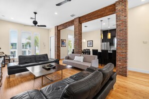 A spacious living area with a modern kitchen and dining space, featuring a large black leather sofa, a grey sofa, and a wooden coffee table.