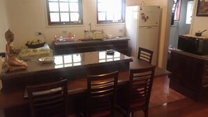 A kitchen with a central island, wooden chairs, a refrigerator, and a Buddha statue. - Apartment in Morro do Elefante Campos do Jordão (Vila Floresta Campos do Jordão)