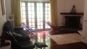 A living room with a fireplace, two lounge chairs, a sofa, and a white rug. - Apartment in Morro do Elefante Campos do Jordão (Vila Floresta Campos do Jordão)