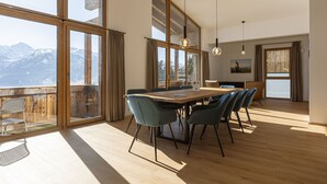 Ein geräumiger Essbereich mit Holztisch und -stühlen, großen Fenstern mit Bergblick und einer modernen Kronleuchter.