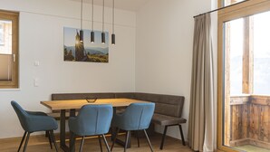 Een eetgedeelte met een houten tafel, vier blauwe stoelen, een bruine bank en een schilderij aan de muur.