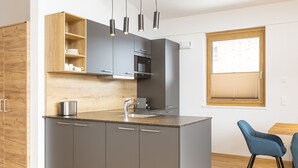 Een moderne keuken met grijze kastjes, een houten aanrechtblad, een ingebouwde magnetron en een raam met zonwering.