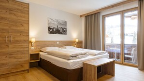 Een slaapkamer met een groot bed, een houten garderobe, nachtlampjes, een bankje en uitzicht op het omliggende landschap door een schuifdeur van glas.