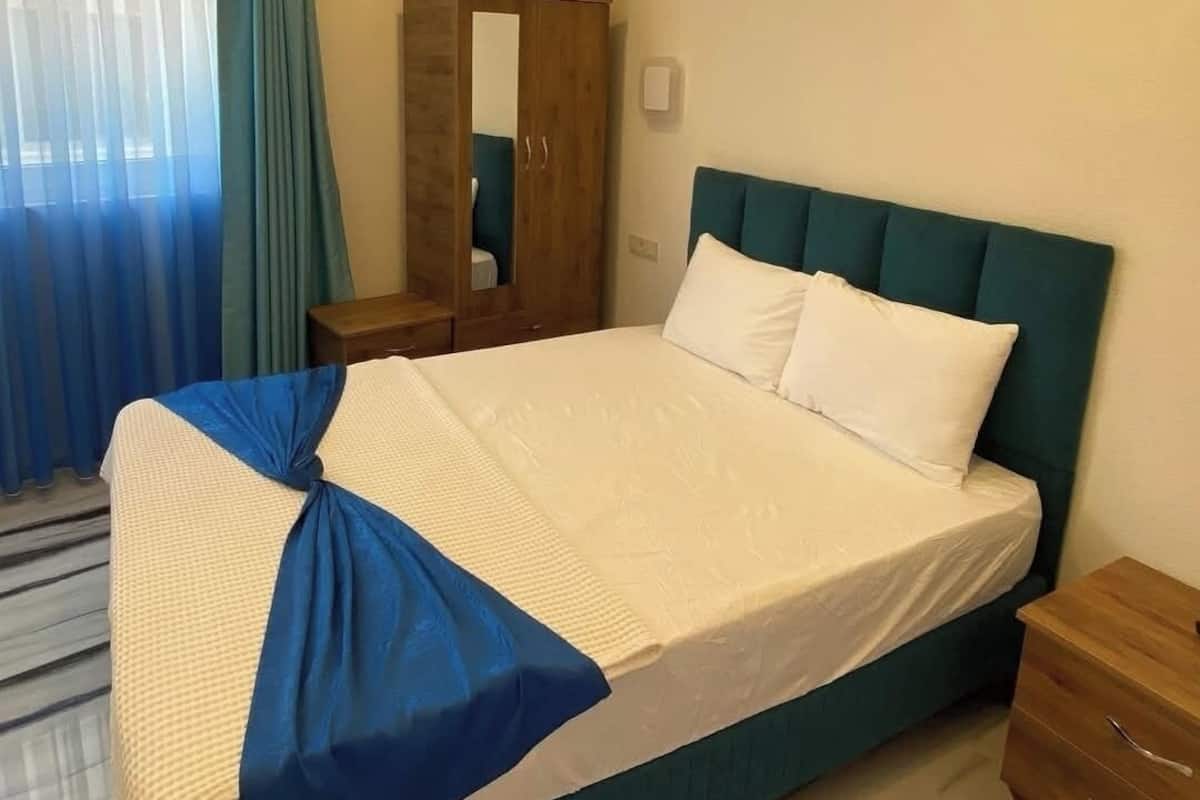 Una habitación de hotel con una cama grande, un armario de madera, un espejo y una ventana con cortinas.