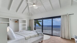 Una camera da letto con un letto, una ventola a soffitto, un armadio e vista sulla spiaggia.