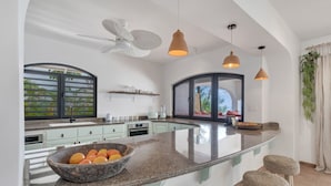 Una cucina moderna con un'isola grande, un ventilatore a soffitto, luci a sospensione e vista sull'esterno.