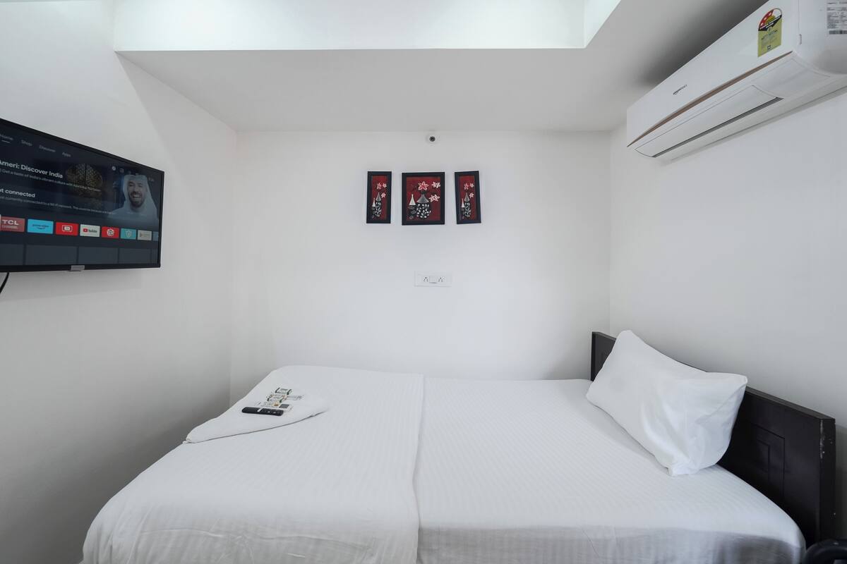 A hotel room with a bed, a TV mounted on the wall, and an air conditioning unit.