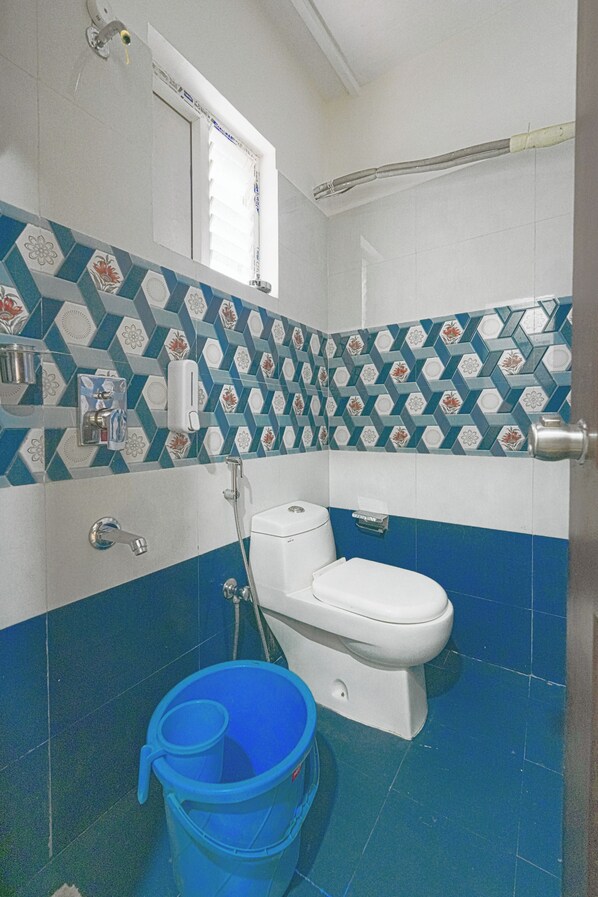 A bathroom with a toilet, a shower, and a blue bucket. - Hivee Hotel (Hyderabad)