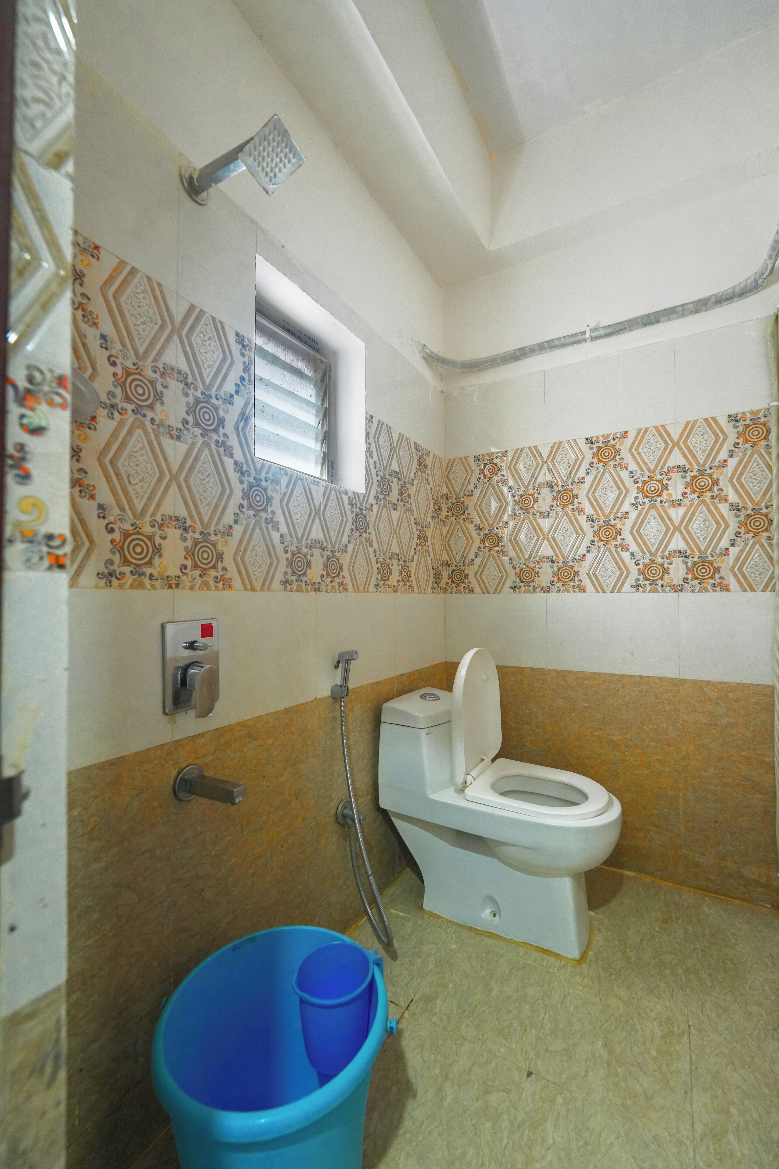 A bathroom with a toilet, shower, and a blue bucket.