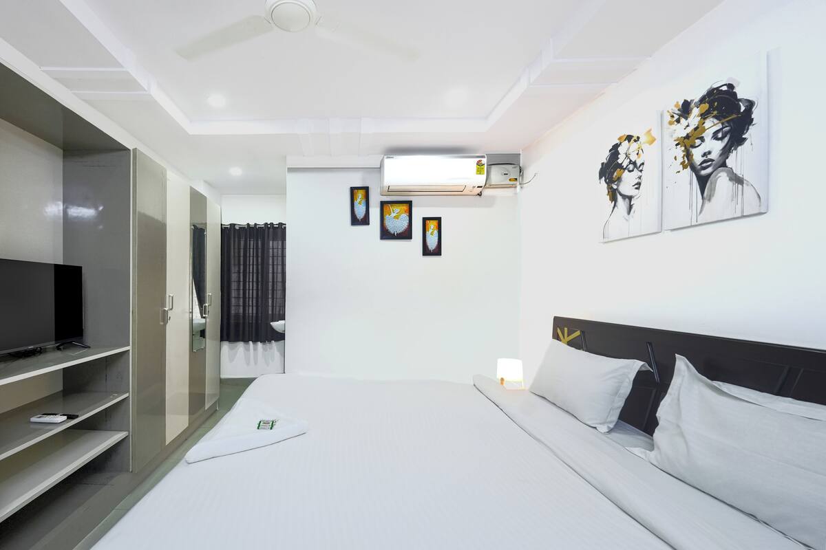 A modern hotel room with a bed, a TV, a wardrobe, and artwork on the walls.