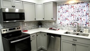 A modern kitchen with stainless steel appliances, white cabinetry, and a backsplash with a kitchen-themed pattern. - Cozy 3-Bed Retreat with Games, Smart TVs & Fire Pit, 12 Mins to Downtown! (Detroit)