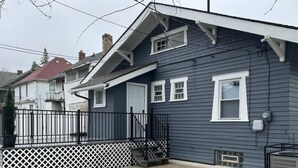 A two-story house with a grey exterior, white trim, and a small front porch. - Cozy 3-Bed Retreat with Games, Smart TVs & Fire Pit, 12 Mins to Downtown! (Detroit)