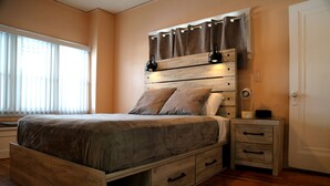 A bedroom with a wooden bed, two bedside tables, and a window with blinds. - Cozy 3-Bed Retreat with Games, Smart TVs & Fire Pit, 12 Mins to Downtown! (Detroit)