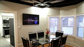 A modern kitchen with stainless steel appliances, a dining area with a glass table and black chairs, and a cityscape view through the windows. - Cozy 3-Bed Retreat with Games, Smart TVs & Fire Pit, 12 Mins to Downtown! (Detroit)